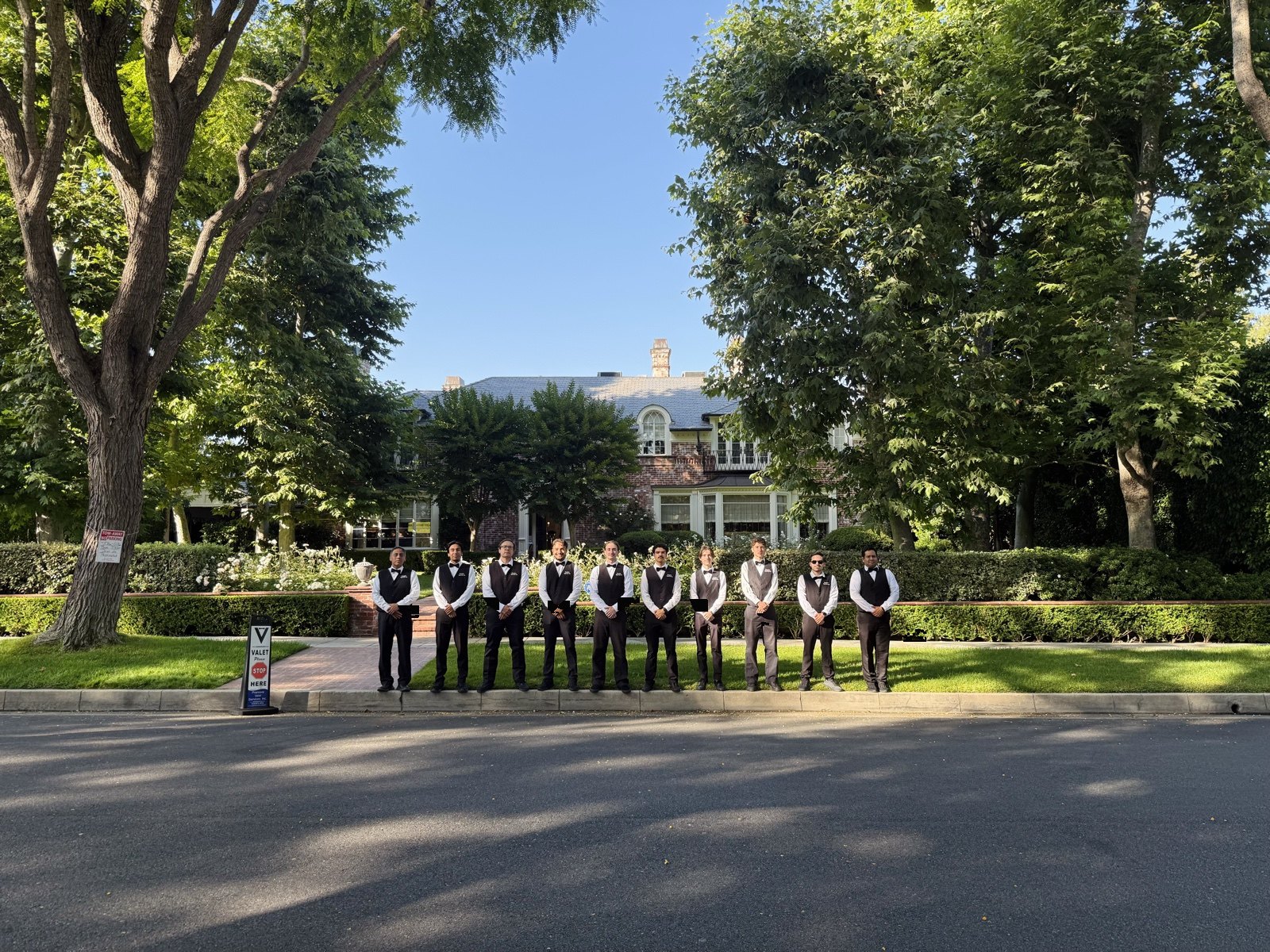 Valet attendants in black vests and bow ties lined up outside a private estate