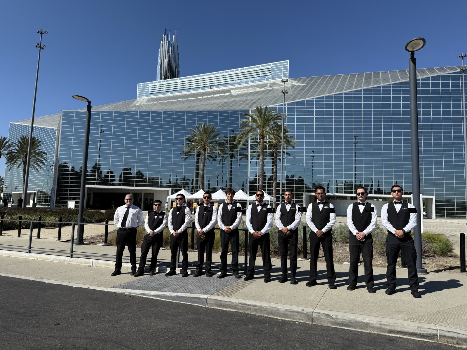 Valet attendants in black vests and bow ties lined up outside a modern event venue